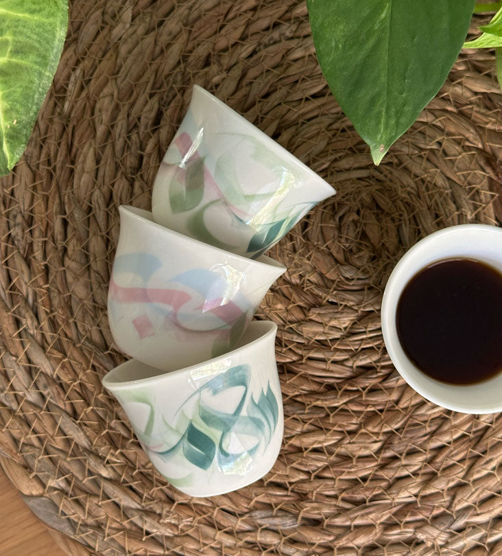 Pastel colored arabic coffee cups featuring Arabic calligraphy done by hand with elegant watercolor brushstrokes